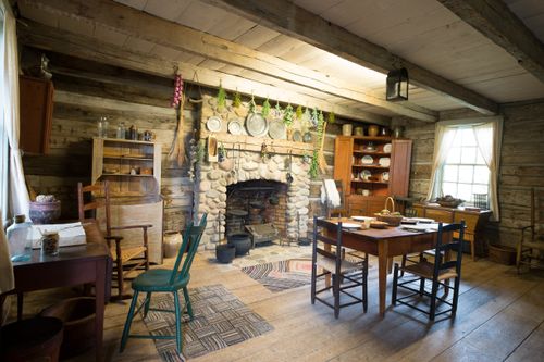 Interior of a log home with a stone fireplace and various old cooking implements