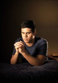 A young man kneeling by his bed in prayer.