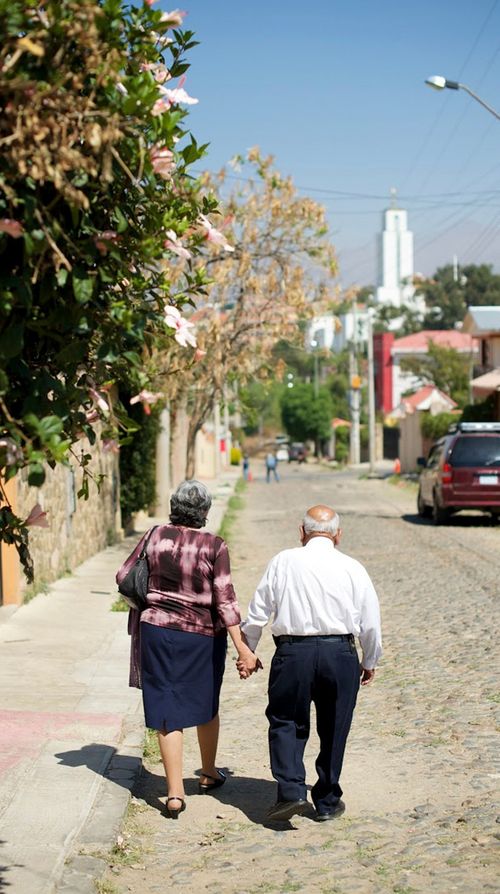 An elderly man and woman holding hands as they walk down a road to the Cochabamba Bolivia Temple in the distance.