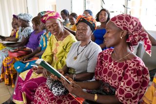 Various women gather together in a church building. They appear to be attending a relief society meeting. They are all sitting as they sing a hymn together. This is in Sierra Leone, Africa.