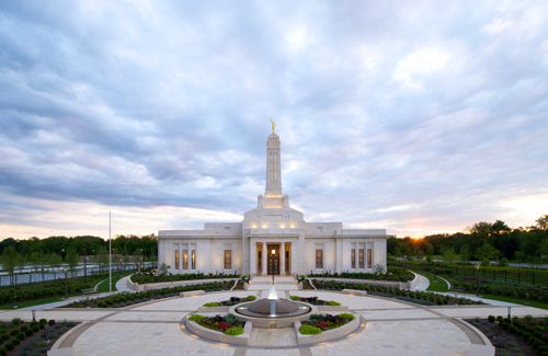 A fountain in front of the Indianapolis Indiana Temple, with clouds and a sunset in the background.