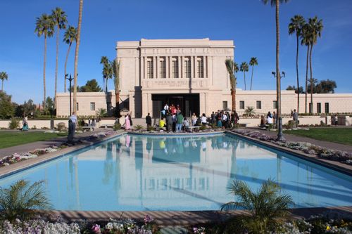 A group of people waiting for a bride and groom to come out of the Mesa Arizona Temple doors, with a clear blue sky overhead.