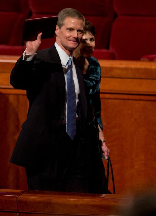 David A. Bednar waving with a journal in his hand as he and his wife exit the Conference Center.
