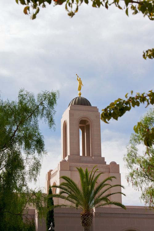 The spire and angel Moroni on the Newport Beach California Temple, with the leaves of nearby trees in the foreground.