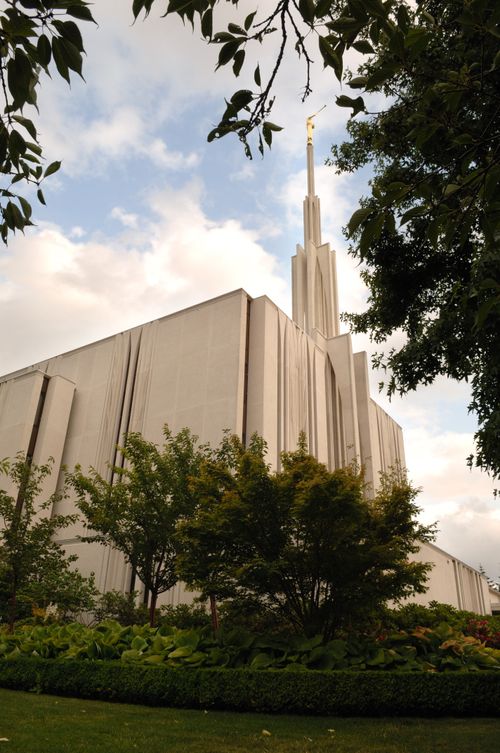 A partial view of the side of the Seattle Washington Temple, with a view of the spire, framed by green trees.
