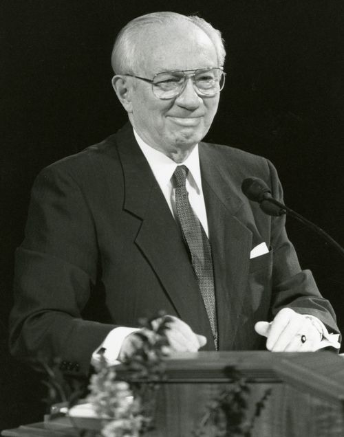 A black and white photo of Gordon B. Hinckley smiling at the pulpit during General Conference.