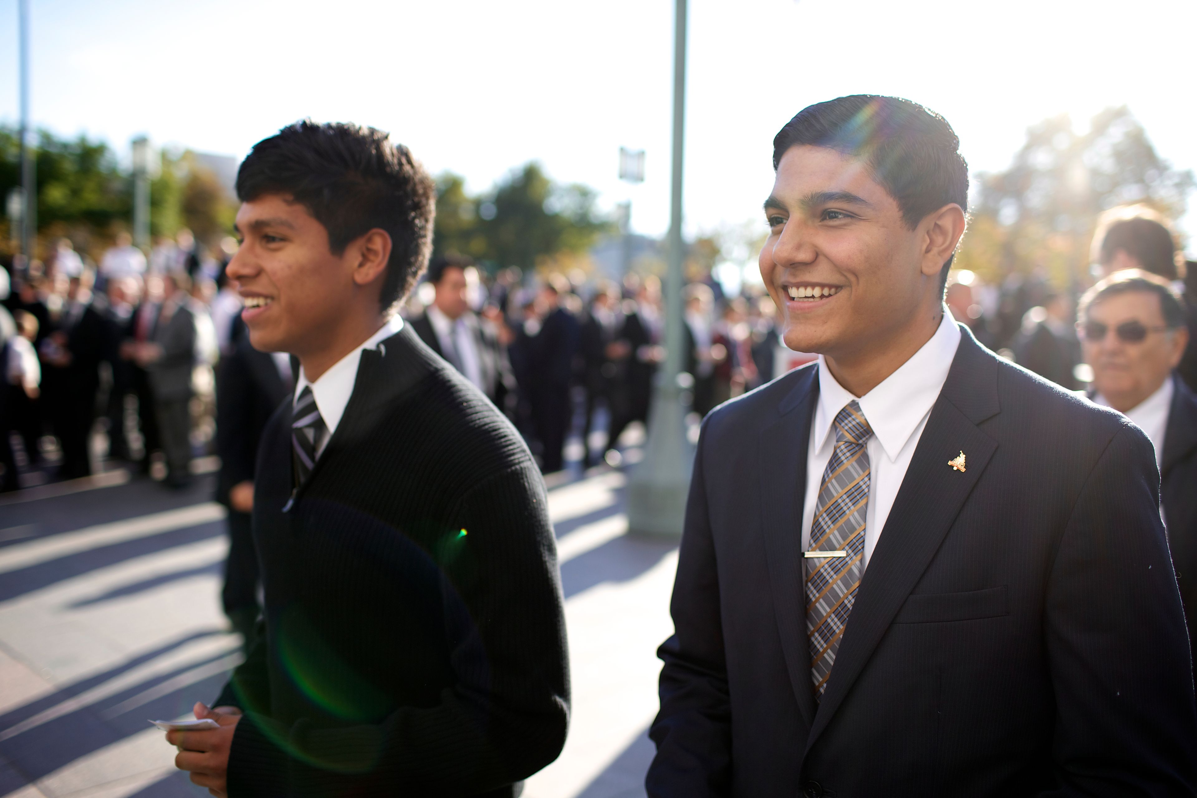 Two young men standing outside with other men while waiting for the priesthood session.  