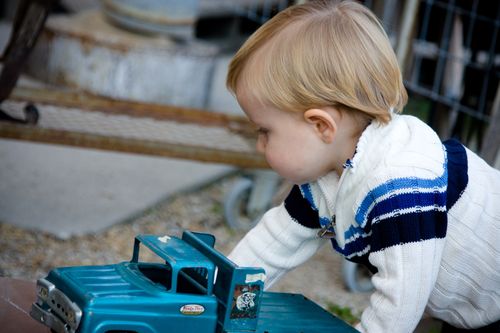 A toddler boy outside playing with a blue truck.