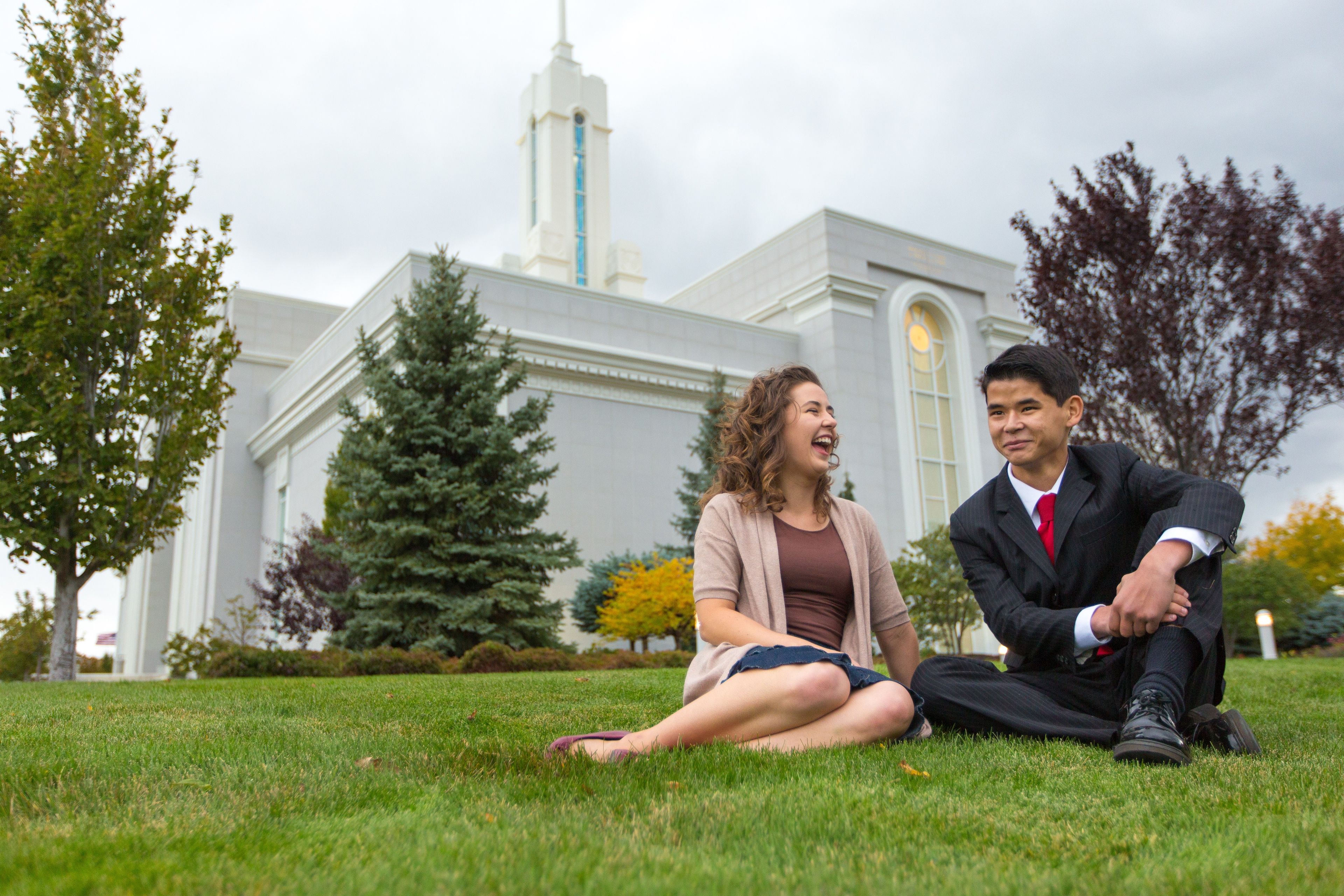 A young man and woman sitting on the grass outside the Mount Timpanogos Utah Temple.