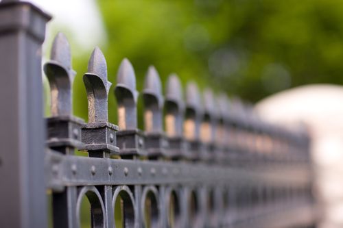 A long row of the decorative tops of the posts on a black iron fence blurring out toward the end of the row.