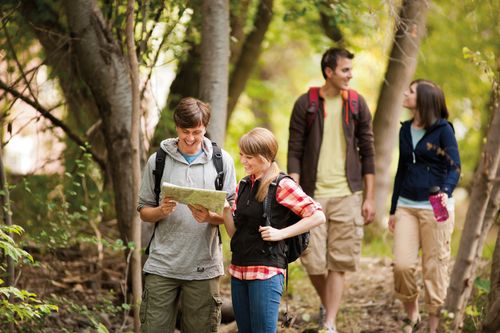 While hiking, one couple stands looking at a map together and another couple talks behind them.