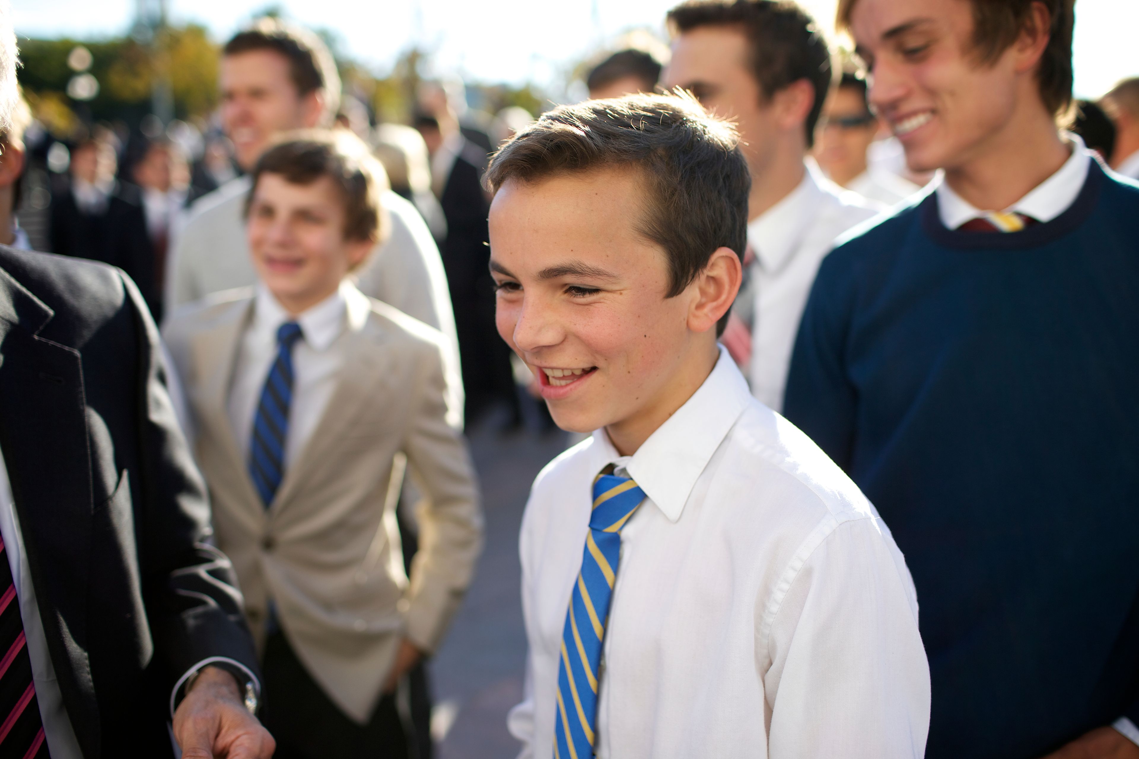 A young man standing and waiting with other young men for the priesthood session.  