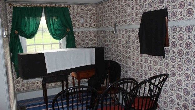 Three chairs facing a coffin in front of a window.