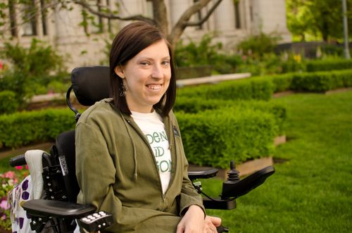 A smiling woman in a wheelchair outdoors.