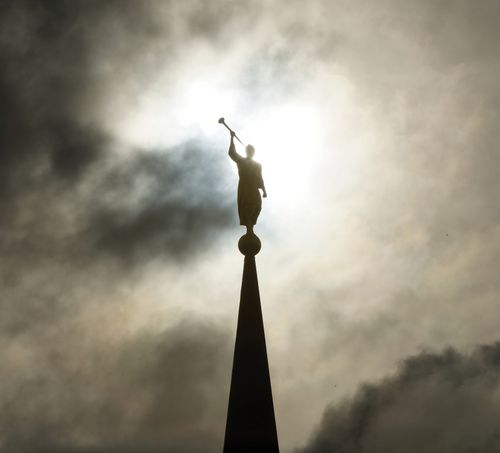 An image of the Angel Moroni on the Star Valley Wyoming Temple, silhouetted against a darkly clouded sky.