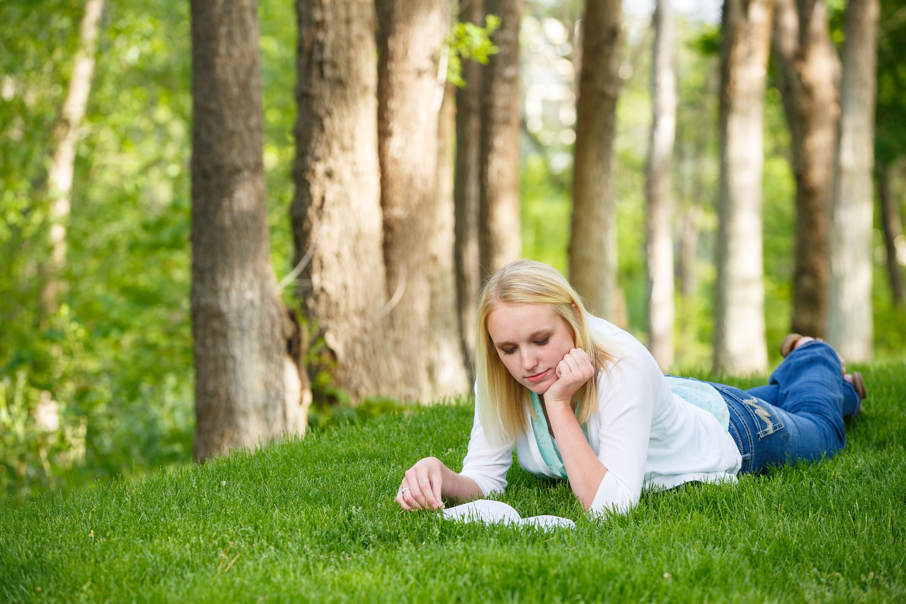 A young woman lying on the grass and reading the Book of Mormon.