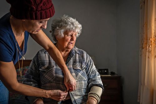 adult woman helps her mother put on clothing