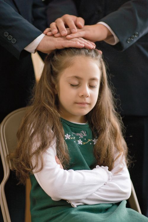 A young girl being confirmed.  Two men are standing behind her with their hands on her head.