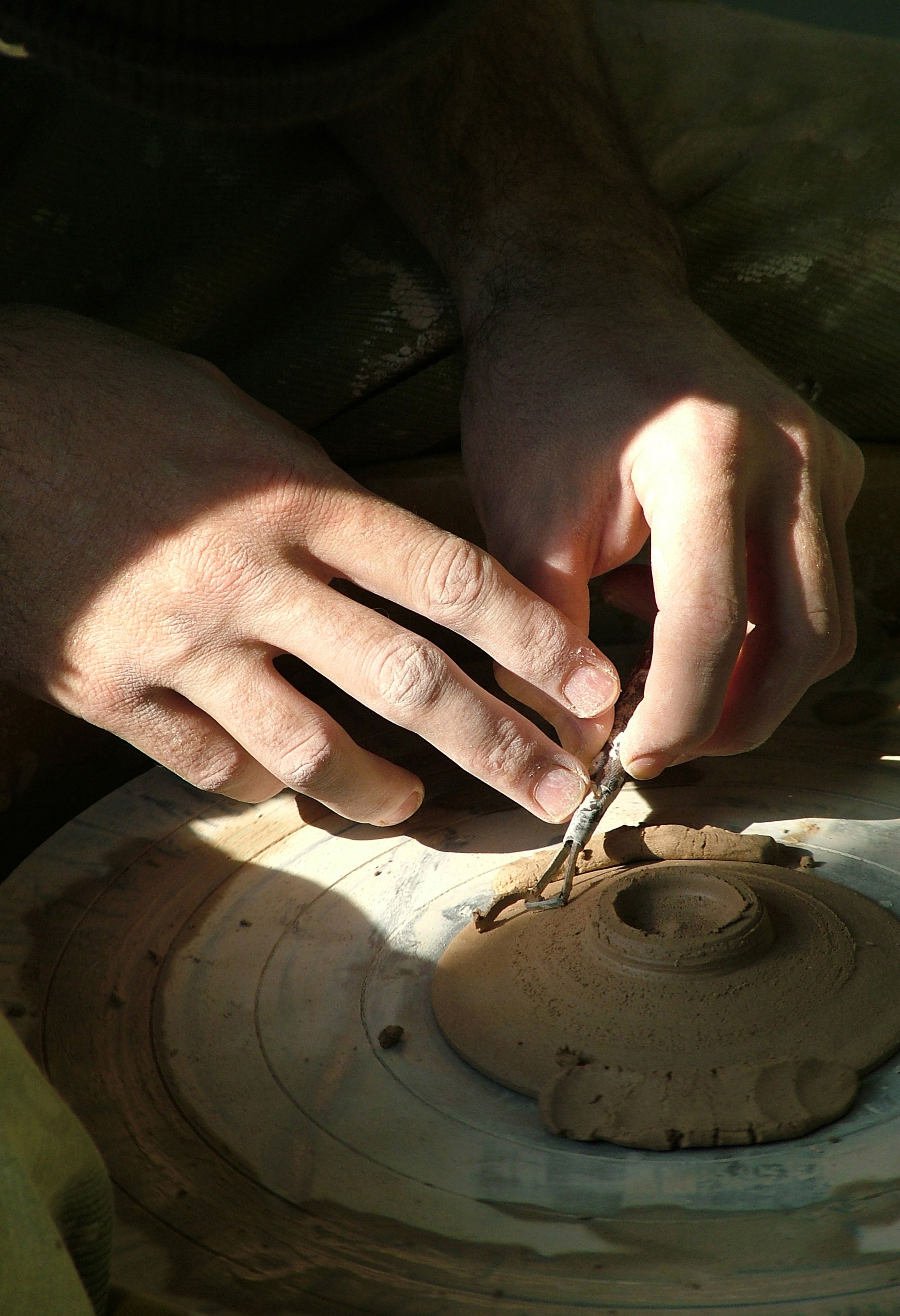 Hands using a tool to sculpt clay.