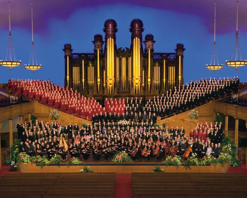 The Mormon Tabernacle Choir with the women in red dresses and the men in black suits, with the orchestra in black in the foreground.