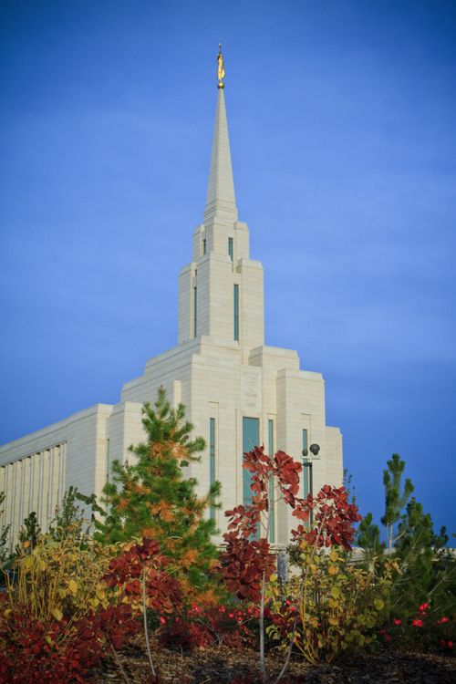 The Oquirrh Mountain Utah Temple on a sunny fall day, with autumn leaves on the trees in the foreground.