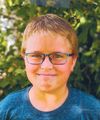 A portrait of a young school boy with glasses and a blue shirt on.