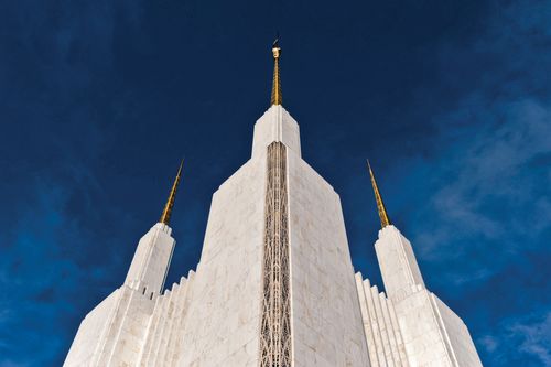 A view of three of the spires of the Washington D.C. Temple, one with the angel Moroni on top, with a dark blue sky behind.