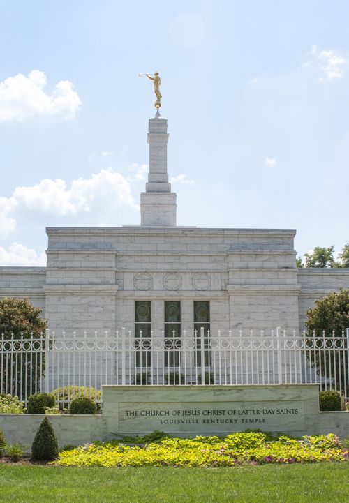 The Louisville Kentucky Temple on a sunny day, with the temple’s granite name sign outside of the temple’s white gate.