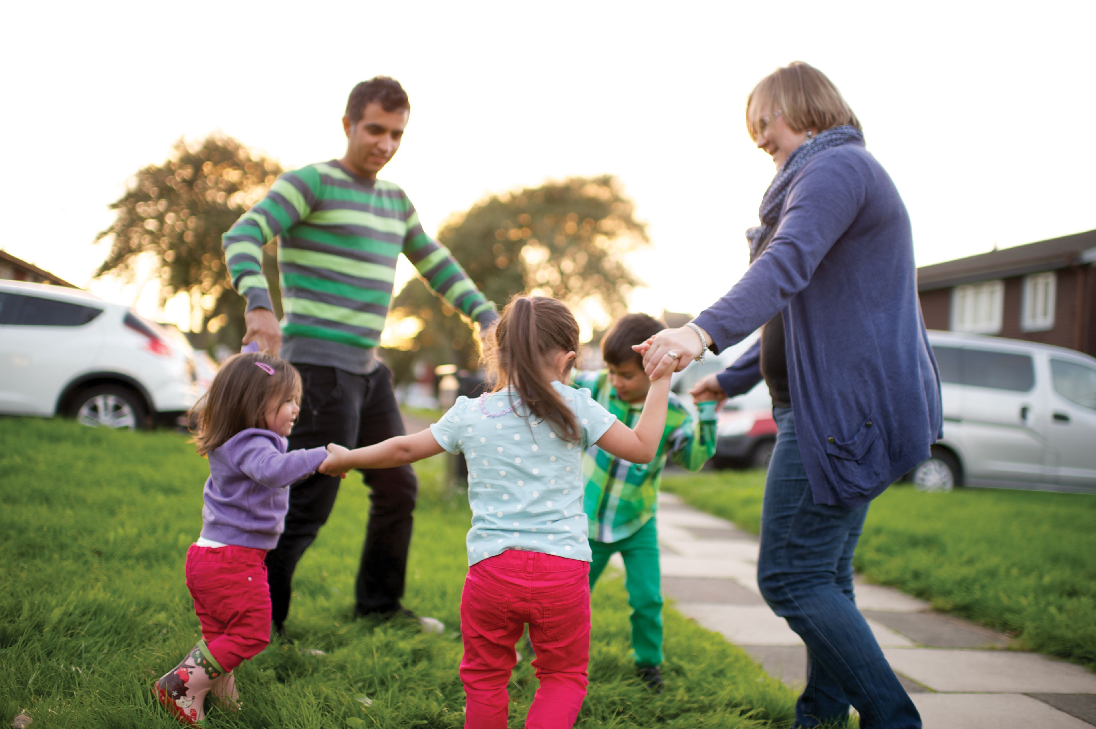 A father and mother playing “Ring around the Rosie” outside with their children.