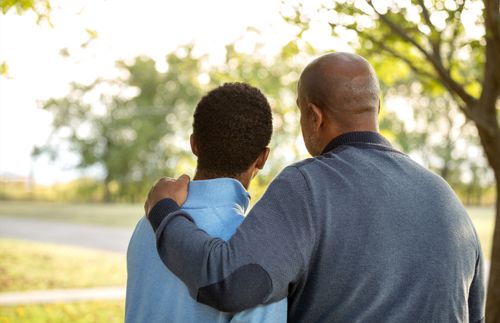 一位父亲把手搭在儿子肩膀上，一起看向远方