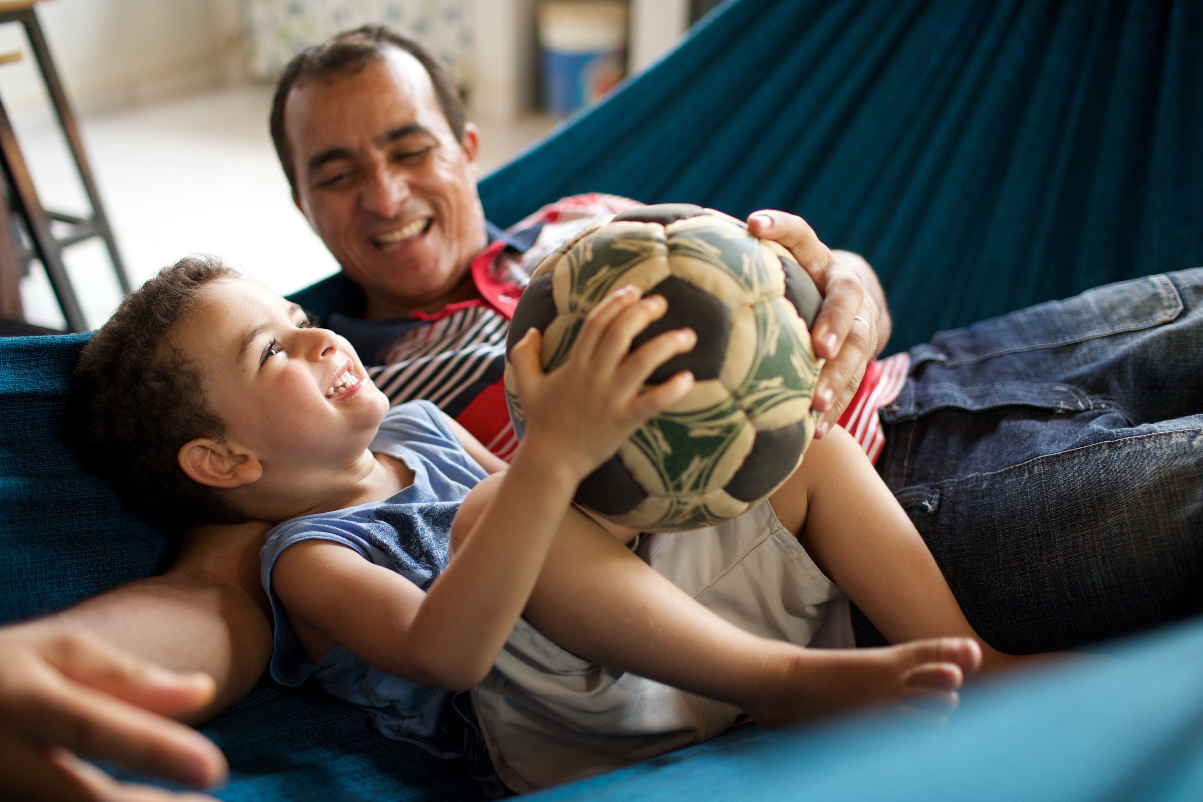 A father and his son sit in a hammock and laugh together.