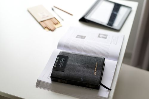 A sister missionary’s badge lying on top of her hardbound scriptures and an open book.