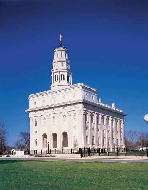 A front side view of the Nauvoo Illinois Temple, with a bright, clear blue sky in the background and green lawns in the front of the temple.
