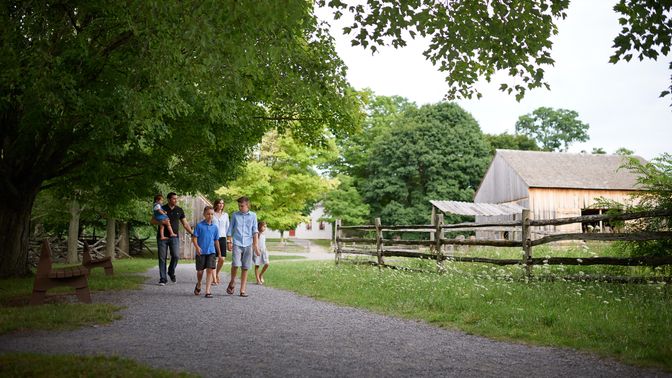 Various people walk the paths around the Sacred Grove. There are lots of trees around and everything is very green. The families are all walking on dirt pathways.