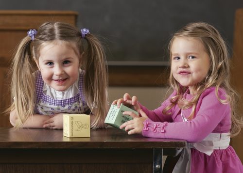 Two young girls standing by a table in Primary.  There are song cubes on the table.
