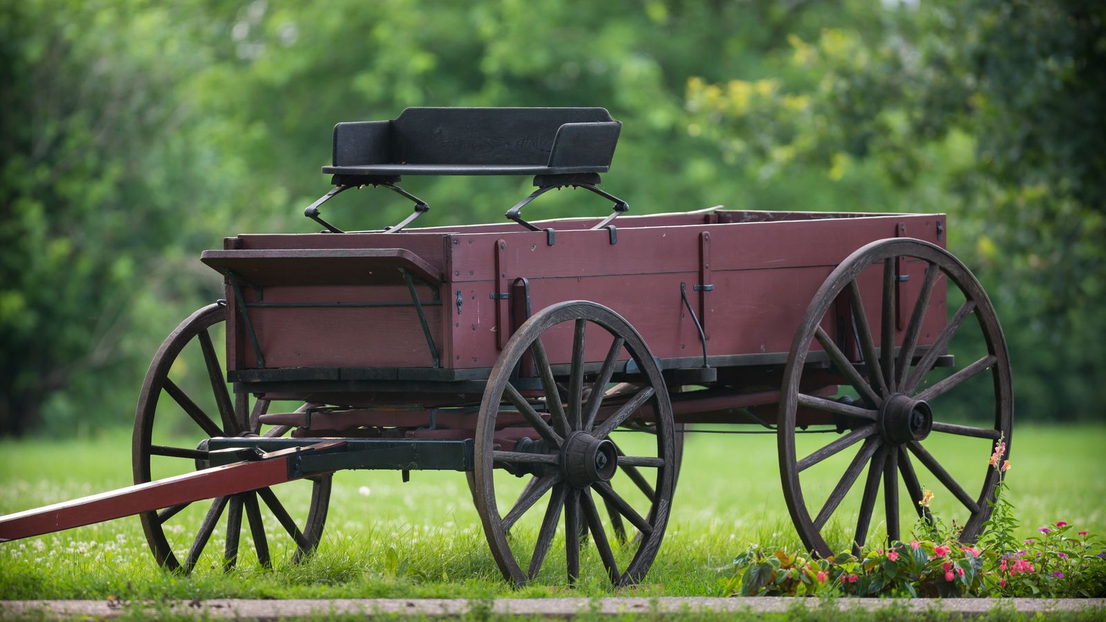 An old red wagon in a field of grass.