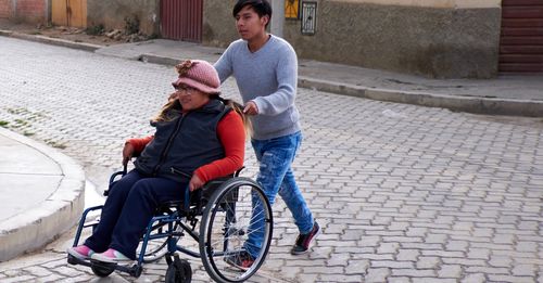 A young man pushing an older woman across the street in a wheelchair.