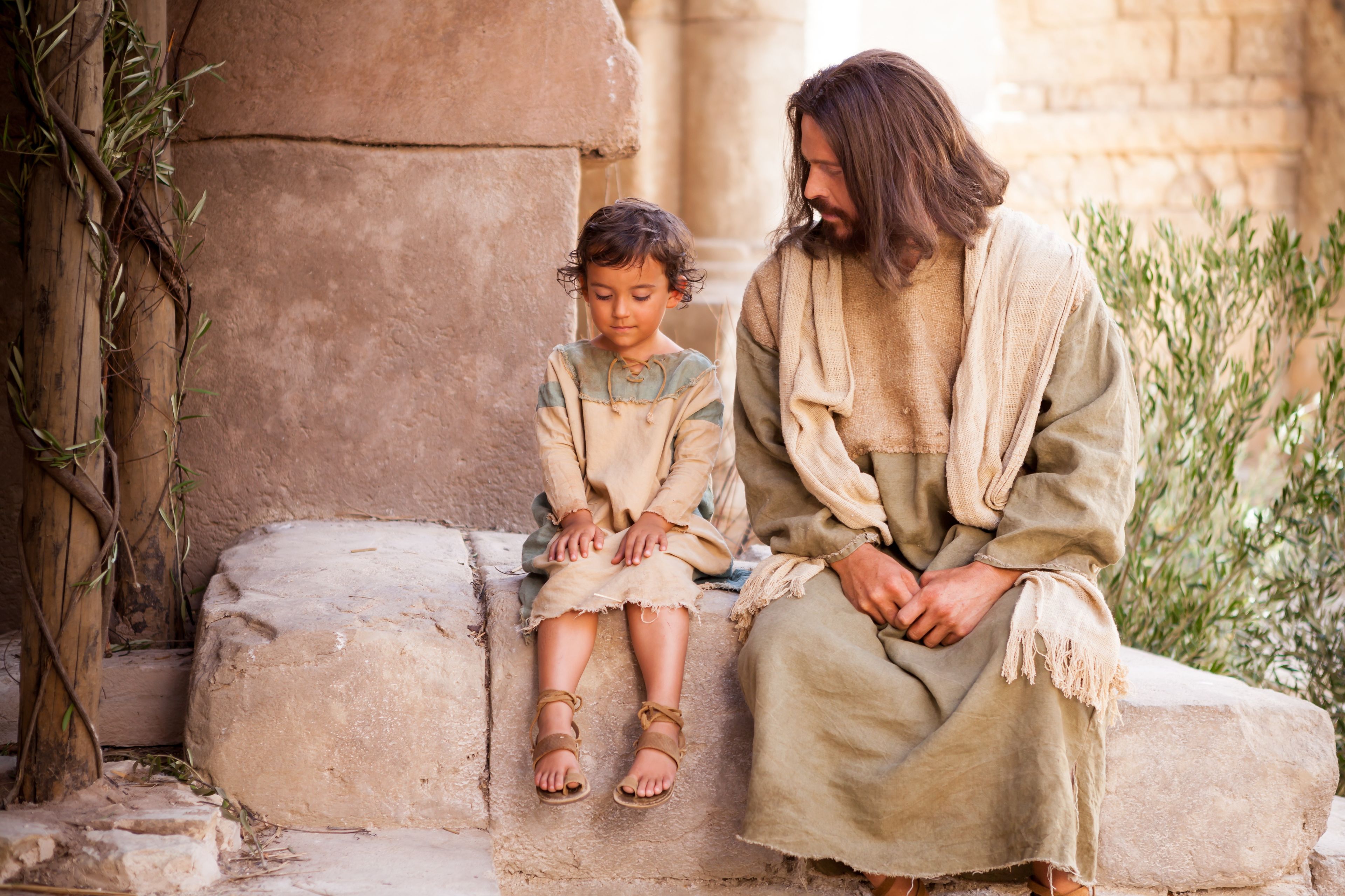 Christ sits with a young child while teaching that we must “become as little children.”