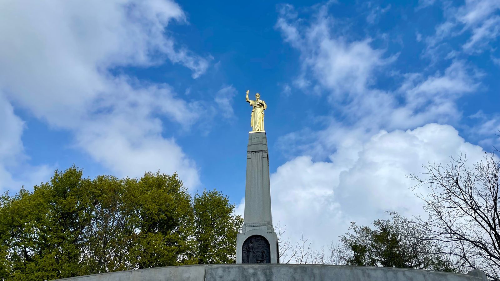 A view of a tall stone piller with a large gold angel on top.