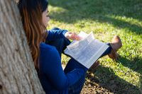 A woman sits under a tree studying the Book of Mormon