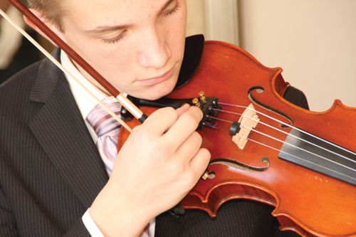 A young man in a suit tuning his violin.