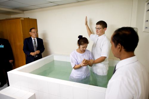 A Thai woman being baptized in a white tile baptismal font.