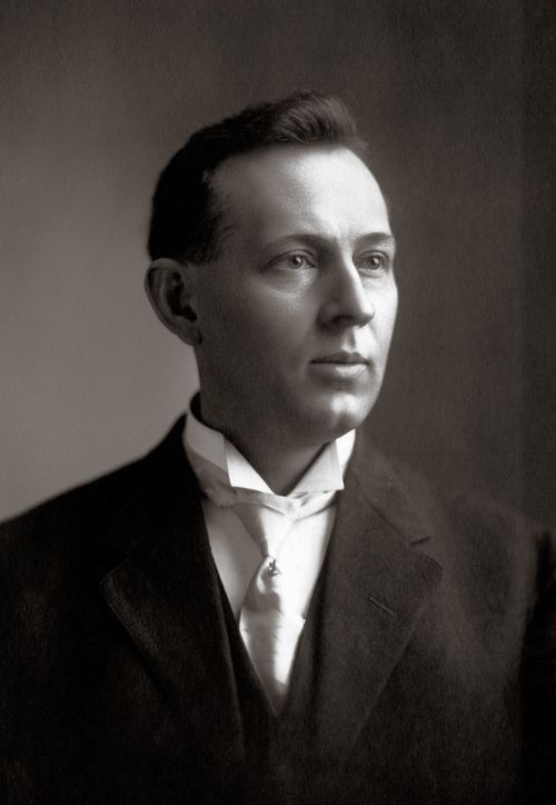 Elder Joseph Fielding Smith in a black suit, white shirt, and white tie, shortly after being ordained an Apostle in 1910.