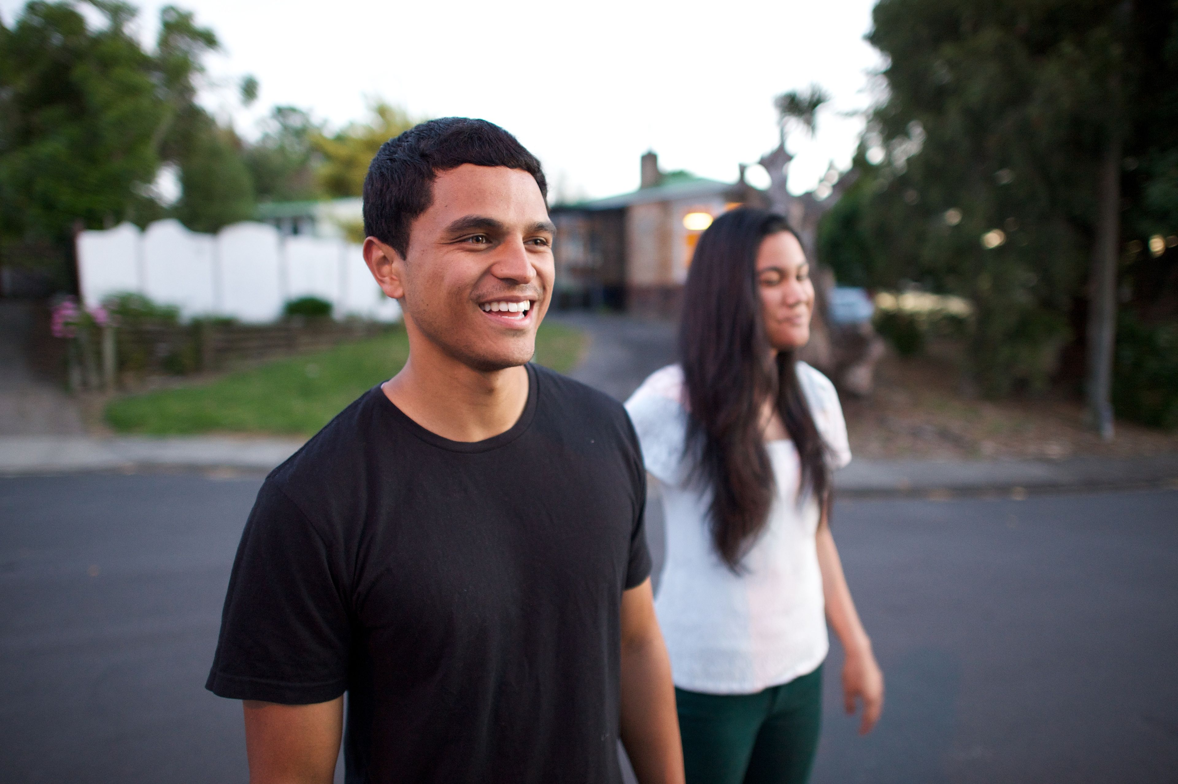 A young man in New Zealand smiles while walking outside next to a young woman.