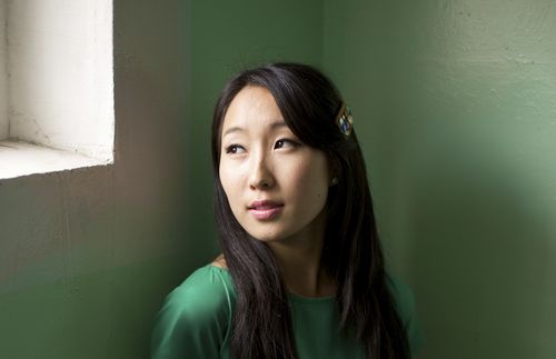 Mongolian young woman standing by a window looking out.