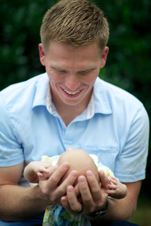 A father looks down with a smile and holds his newborn baby.
