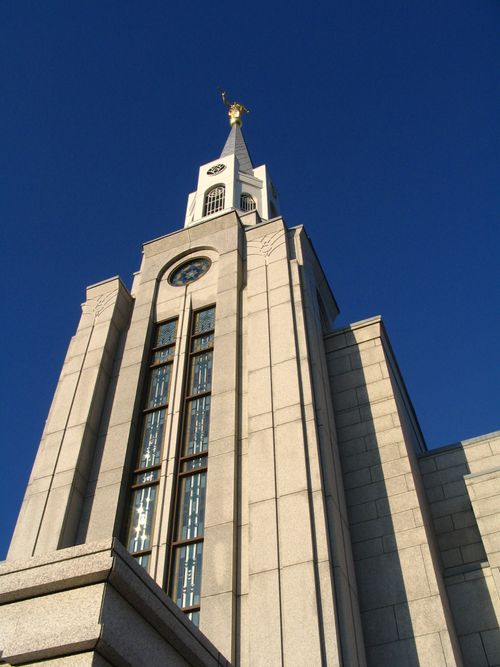 A view of the Boston Massachusetts Temple spire from below, with a blue sky behind it.