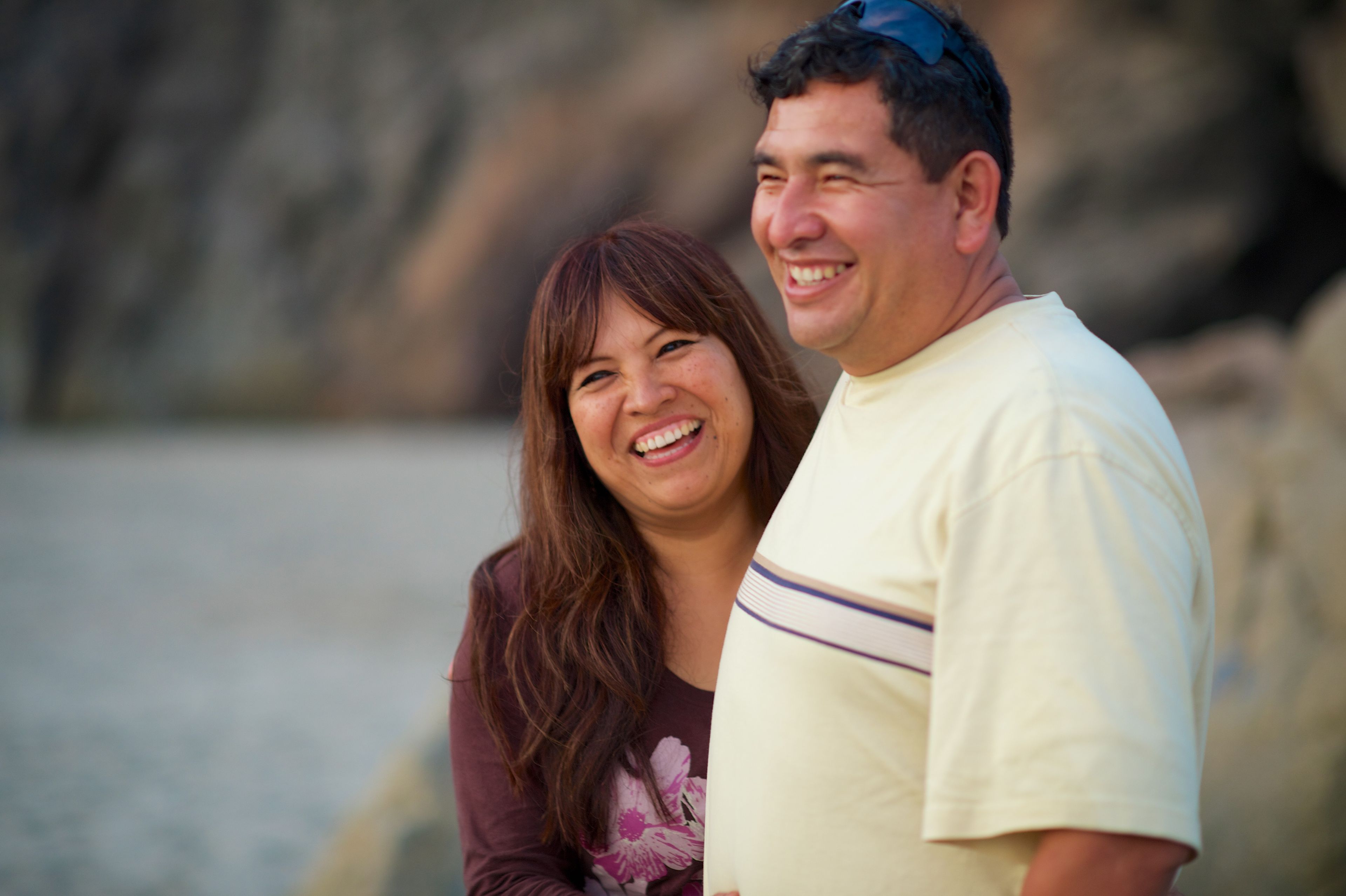 A woman smiles while standing by her husband on a beach.