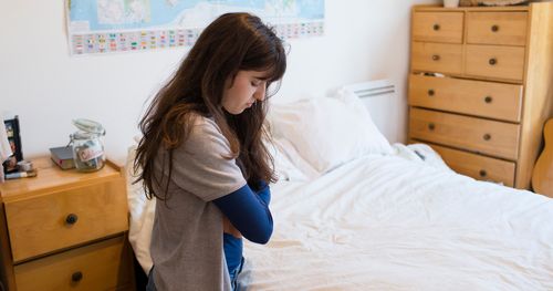 A young woman prays by her bedside.