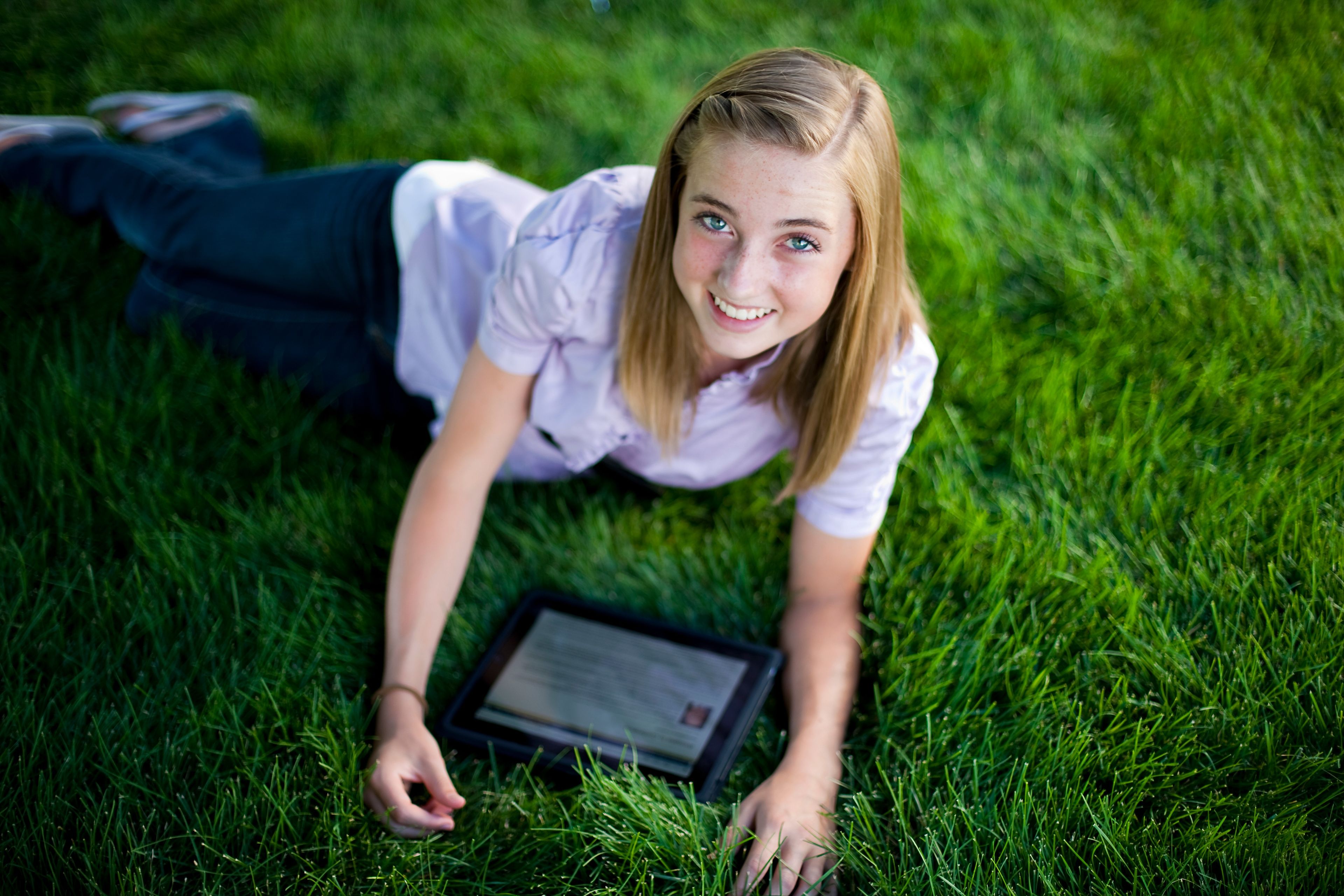 A young woman on the grass outside, using a tablet.